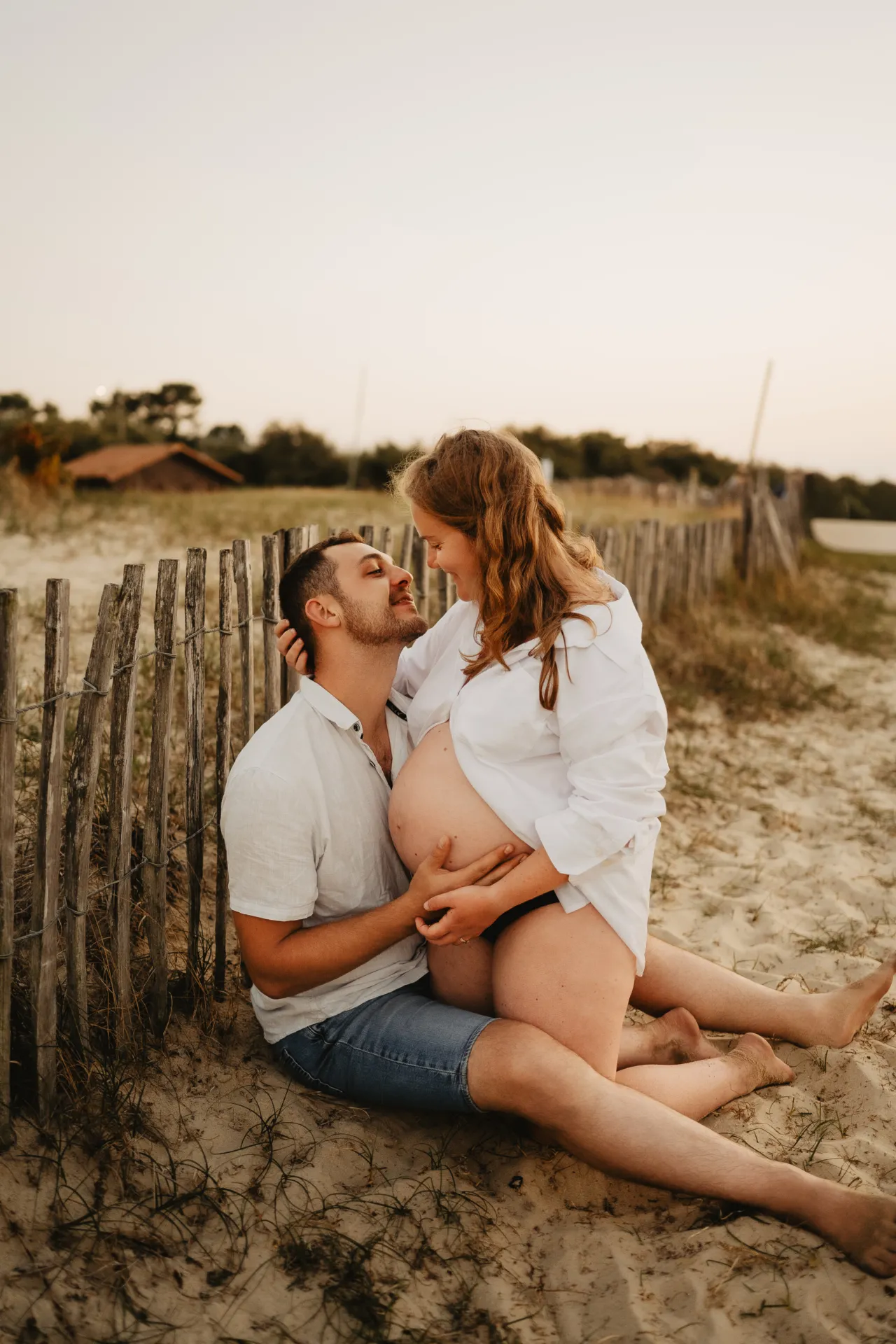 Future maman assise dans l'herbe haute au soleil couchant