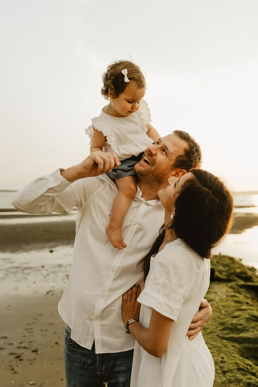 Parents et enfant les pieds dans l'eau au soleil couchant